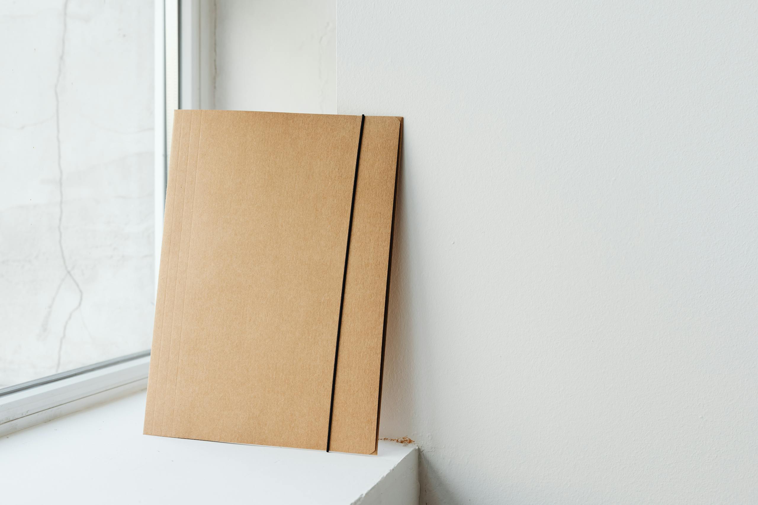 A simple cardboard folder placed by a window, ideal for creative mockups.